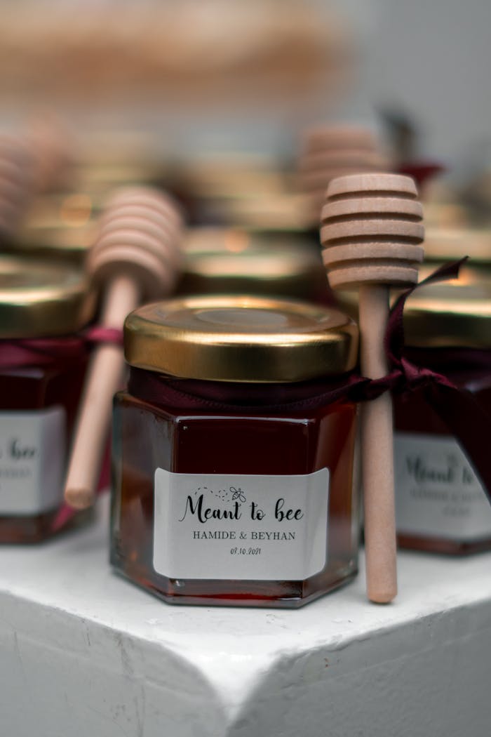 Close-up of honey jars tied with ribbons, accompanied by honey dippers, labeled Meant to Bee.